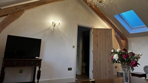 A room with a chandelier, a flat-screen TV, a skylight, and a vase with flowers.