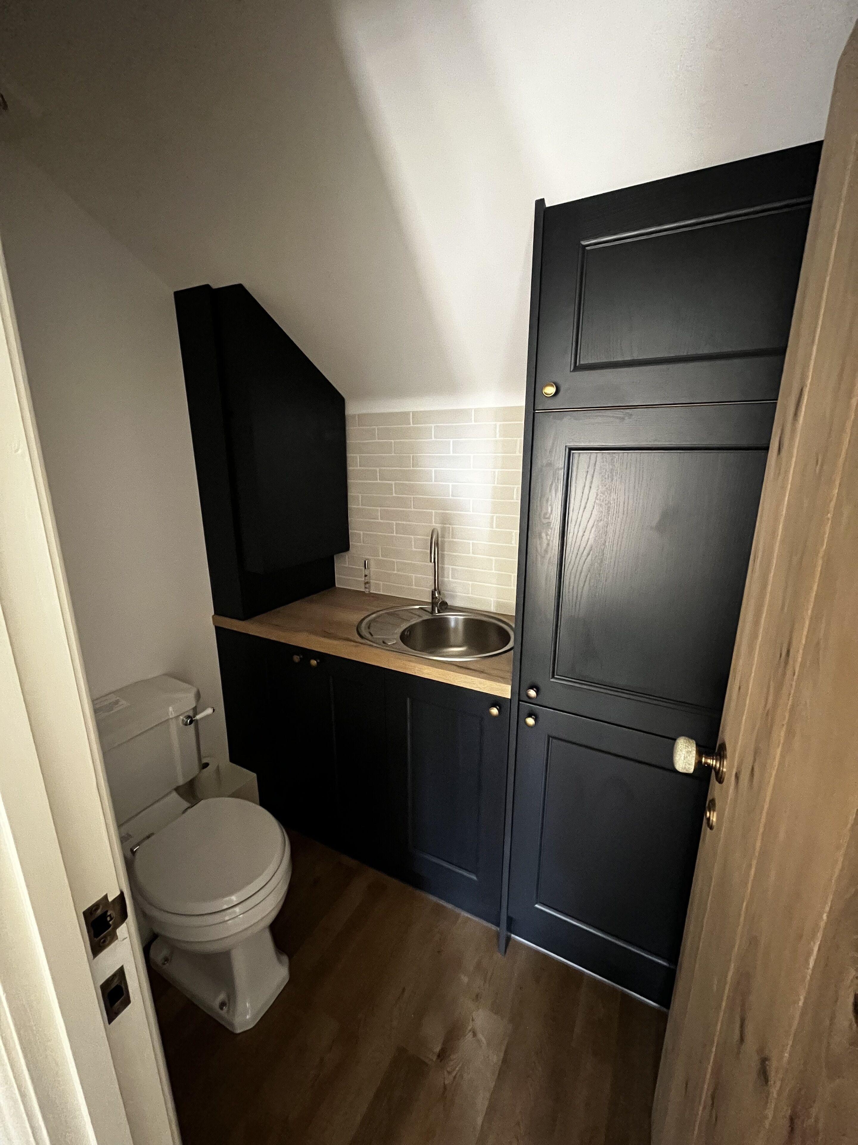 Een kleine keuken met een spoelbak, toilet en donkere keukenkastjes.