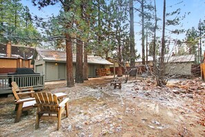 A rustic cabin with a deck, surrounded by tall pine trees.