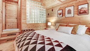 Un dormitori de cabana de fusta amb un llit gran, una finestra amb vidre motllurat i quadres amb marc a la paret.