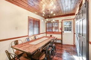 A dining area with a wooden table and chairs, wooden ceiling beams, and a door with a sign above it.