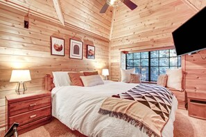 Un dormitorio de cabaña de madera con una cama, mesitas de noche y un televisor.