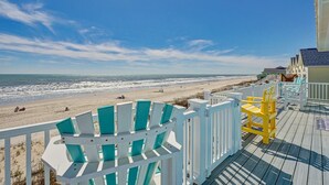 Blick auf einen Strand von einer Terrasse mit weißen Geländern und bunten Adirondack-Stühlen.