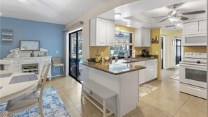 Een moderne keuken met witte kasten, een centraal eiland en een eethoek met een tafel en stoelen.