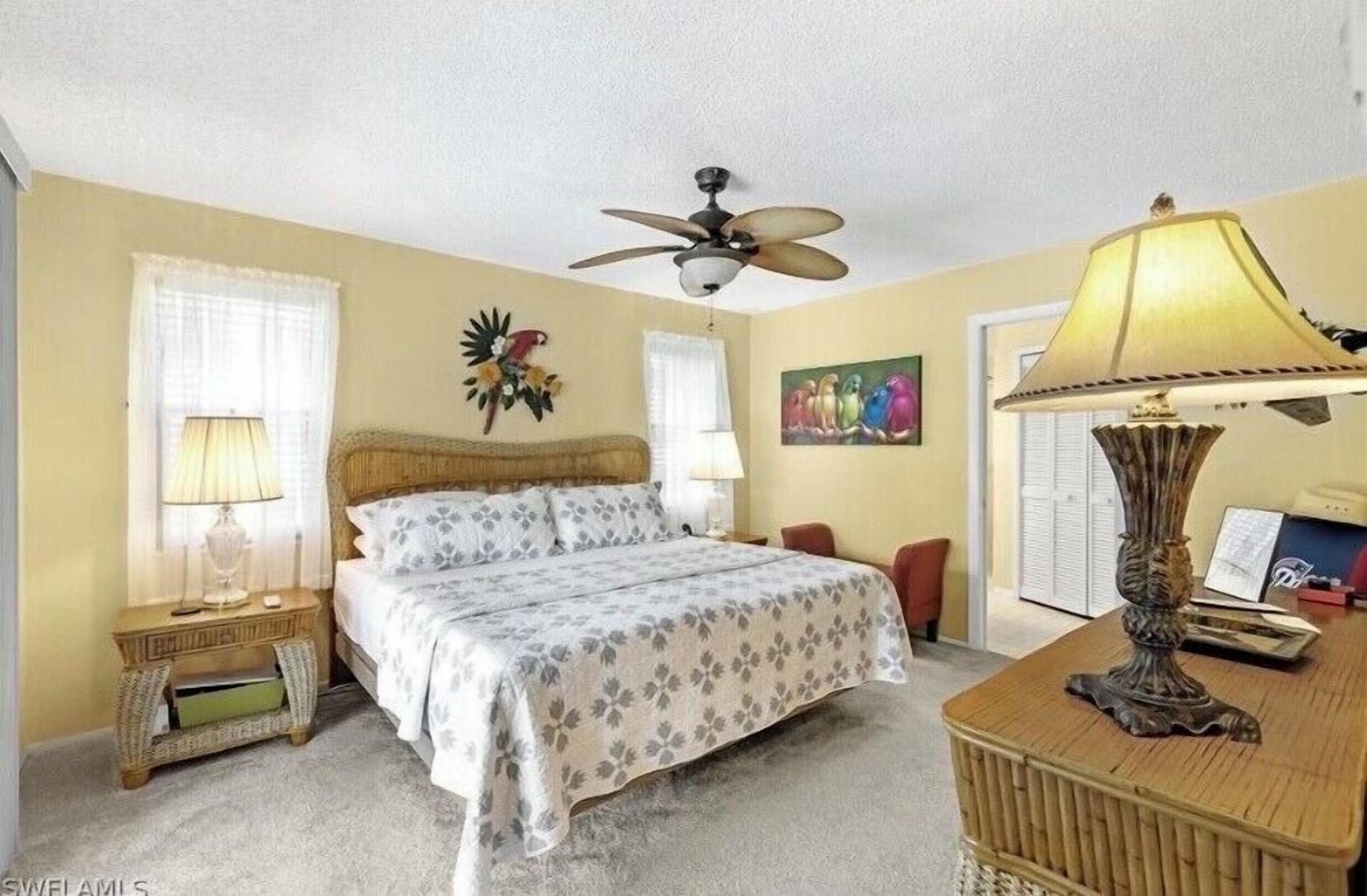 A bedroom with a bed, two bedside tables, a desk, a chair, a ceiling fan, and a lamp.