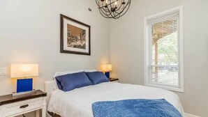 A bedroom with a bed, two bedside tables with lamps, a framed picture on the wall, and a window with blinds. - Medical District Gem i (Chicago)