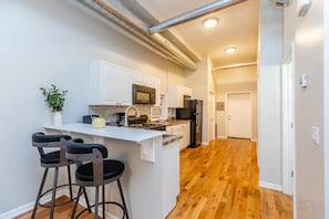 A modern kitchen with a central island, bar stools, and a view into the dining area. - Medical District Gem i (Chicago)