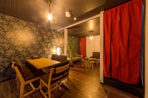 A room with a wooden dining table, chairs, a red curtain, and a patterned wall.