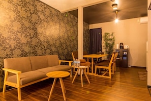 Un salon confortable avec un canapé et une table basse, une table à manger avec des chaises, et un coin cuisine équipé d’un réfrigérateur et d’une machine à café.