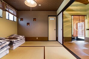 A traditional Japanese room with tatami flooring, a low ceiling, and a sliding door leading to another room.