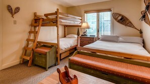 Une chambre avec un lit superposé, une échelle, une table de chevet avec une lampe et une fenêtre avec des stores.