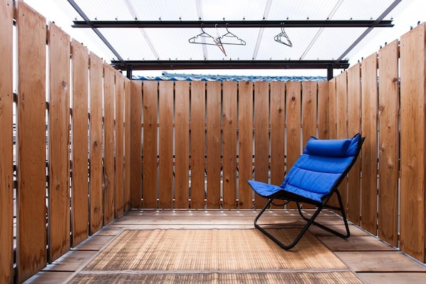 A wooden room with a blue chair, a bamboo mat, and a metal ceiling structure.