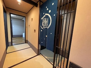 A hallway with tatami mats, a shoji screen with a geometric design, and a sliding door with a metal handle.