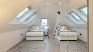 Ein modernes, helles Schlafzimmer im Dachgeschoss mit Dachfenstern, zwei Betten und einem großen Spiegel.