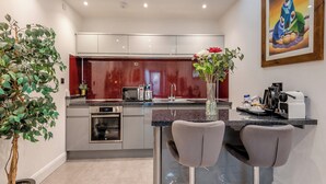 Eine moderne Küche mit integriertem Backofen, Mikrowelle und Kaffeemaschine. Auf der Arbeitsfläche befinden sich zwei Barhocker und eine Vase mit Blumen.