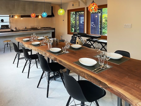 A modern kitchen with a long wooden table set for dining, black chairs, and colorful pendant lights.