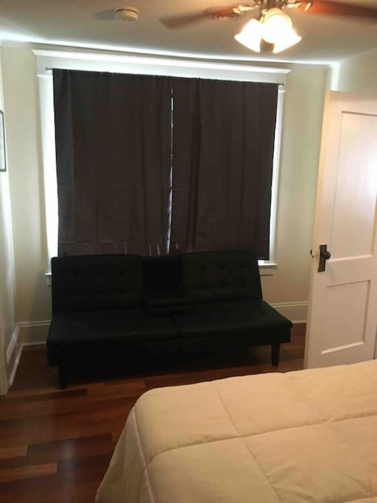 A room with a bed, a dark-colored sofa, a window with curtains, and a door.