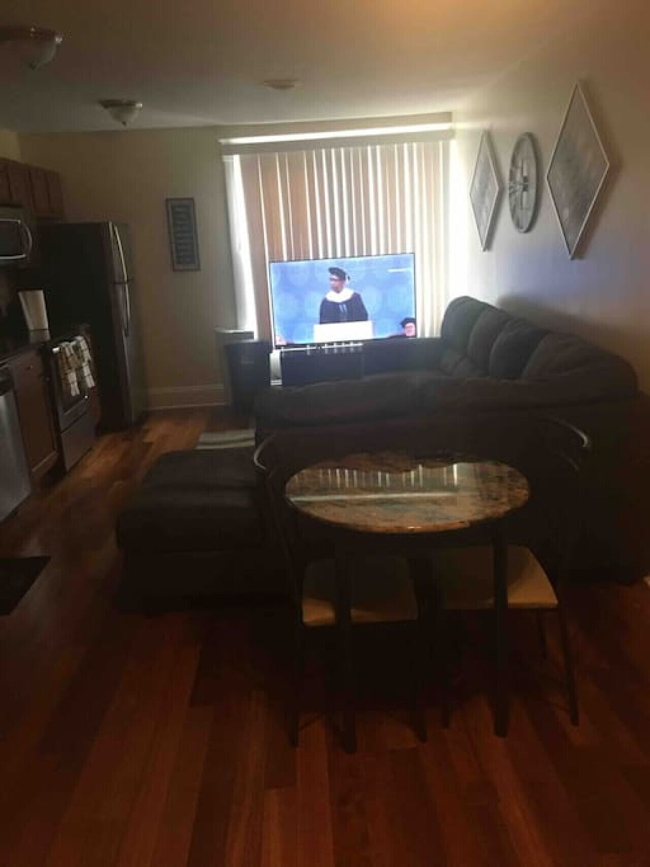 A living room with a television, a sofa, a dining table, and a kitchen area with cabinets and appliances.