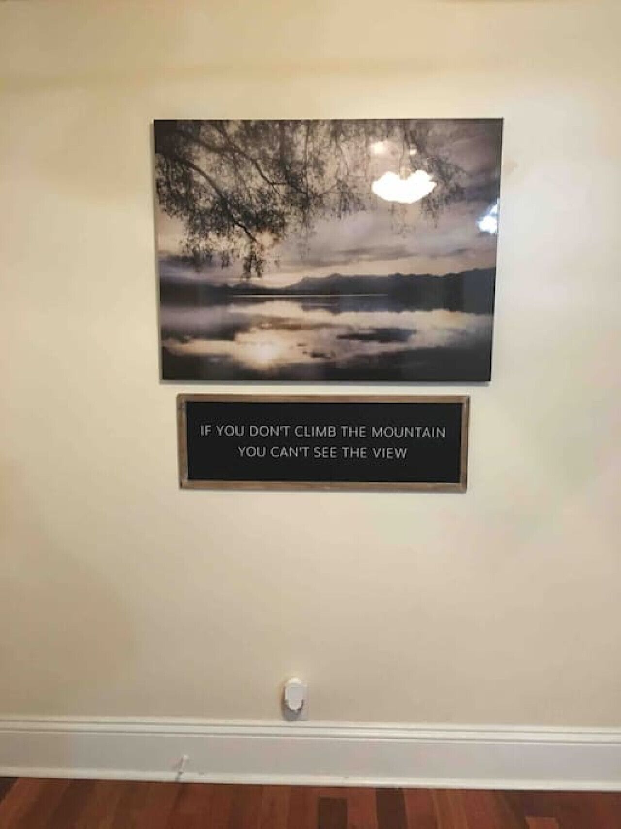 A framed quote on a wall with a landscape painting above it.
