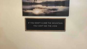 A framed quote on a wall with a landscape painting above it.