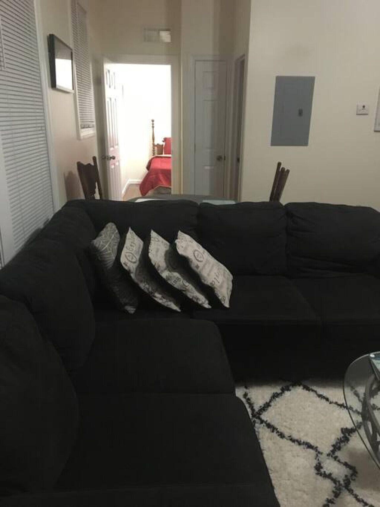 En sort modulsofa med mønstrede puder, en hvid måtte med et sort geometrisk mønster, og en dør der fører til et andet rum.