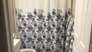 A bathroom with a toilet, a shower curtain with a floral pattern, and a small mat on the floor. - The couples home with free wifi (Schenectady)