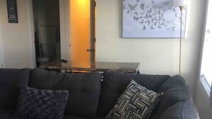Una sala de estar con un sofá seccional gris oscuro, un cojín estampado y una obra de arte abstracta colgada en la pared.