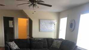 Una sala de estar con un sofá modular, un ventilador de techo, una alfombra y pisos de madera.