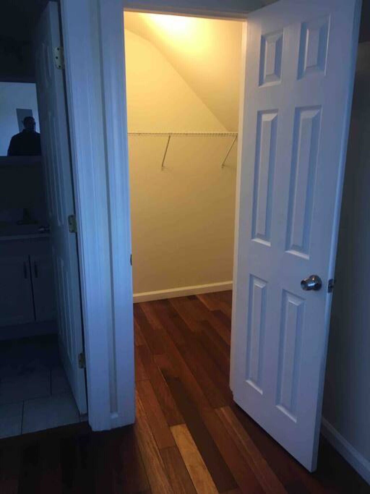 Una habitación con piso de madera, una puerta blanca y un armario con ropa colgada.
