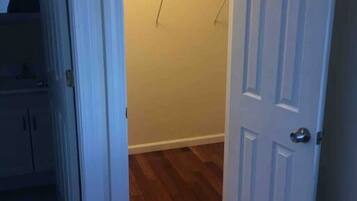 Una habitación con piso de madera, una puerta blanca y un armario con ropa colgada.