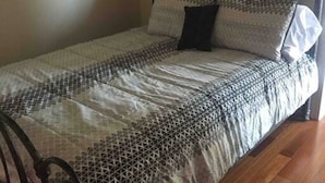 Una cama individual con estructura metálica, un edredón estampado y dos almohadas.