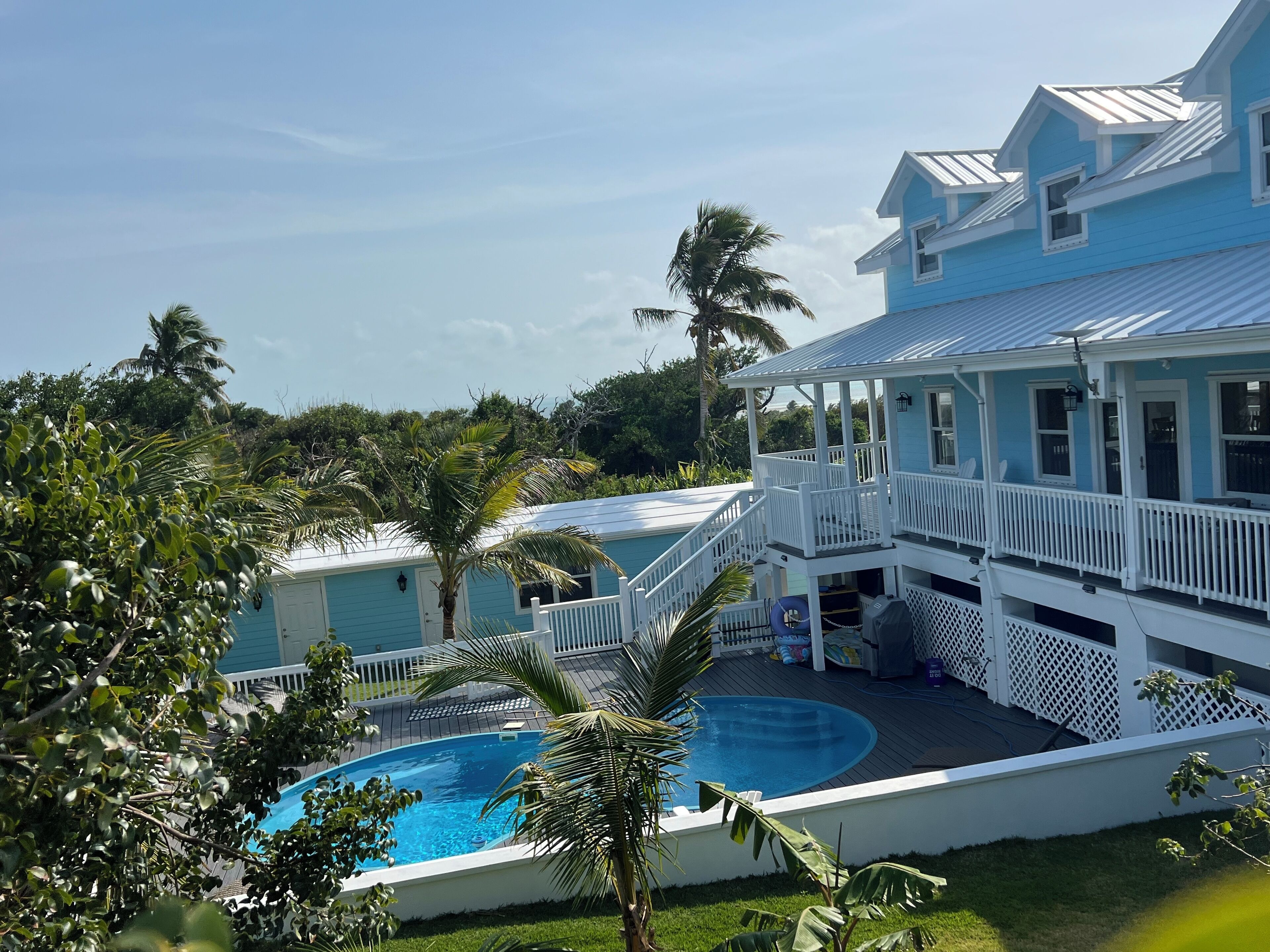A two-story house with a pool, surrounded by palm trees and a clear sky.