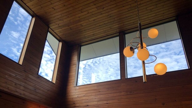 Ein Zimmer mit Holzwänden und -decke, großen Fenstern und einer hängenden Leuchte.