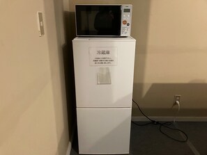 Un refrigerador blanco con un microondas encima, un cable de alimentación y un cartel con texto en japonés.