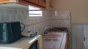Una cocina con gabinetes de madera, microondas, estufa a gas y un lavamanos.