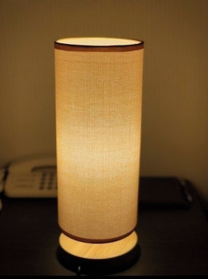 Lampada cilindrica con paralume in tessuto texturizzato su una superficie nera.