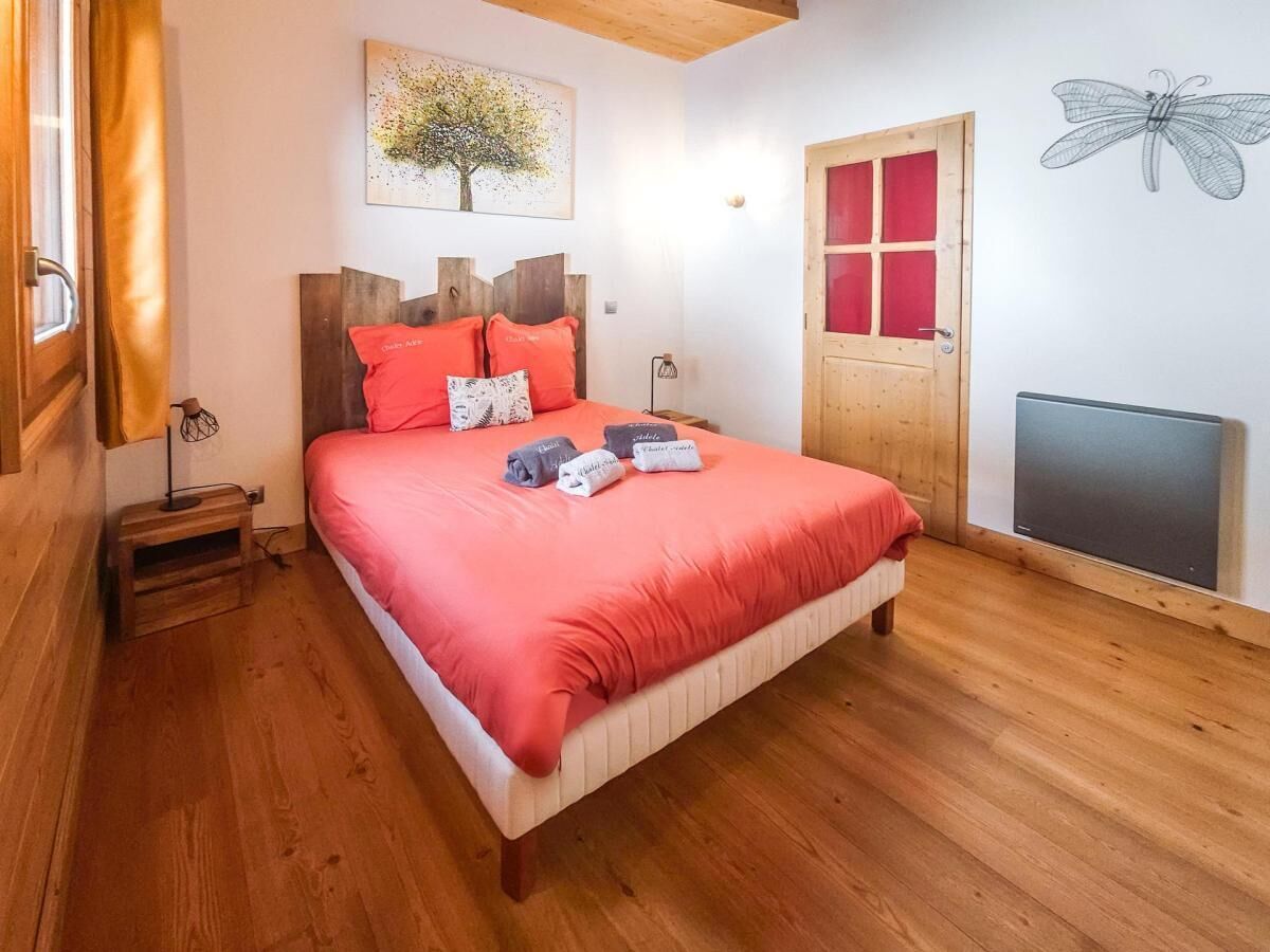 A bedroom with a wooden bed, red bedding, a wooden headboard, a wall-mounted artwork of a tree, a red-framed door, and a radiator.