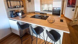 Una cocina moderna con detalles de madera, una isla central con taburetes de bar y una lámpara colgante.