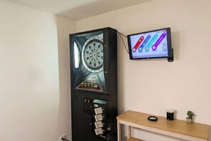 Un jeu de fléchettes doté d’un tableau de pointage numérique et une petite table sur laquelle se trouvent une plante et une tasse.