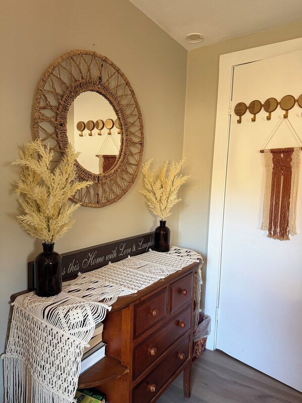 A room with a wooden dresser, a mirror with a macramé frame, and a macramé wall hanging.