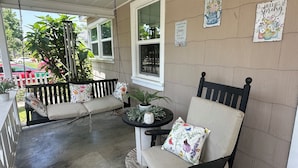 Une véranda avec une balançoire, une chaise et une petite table sur laquelle est posée une plante en pot.