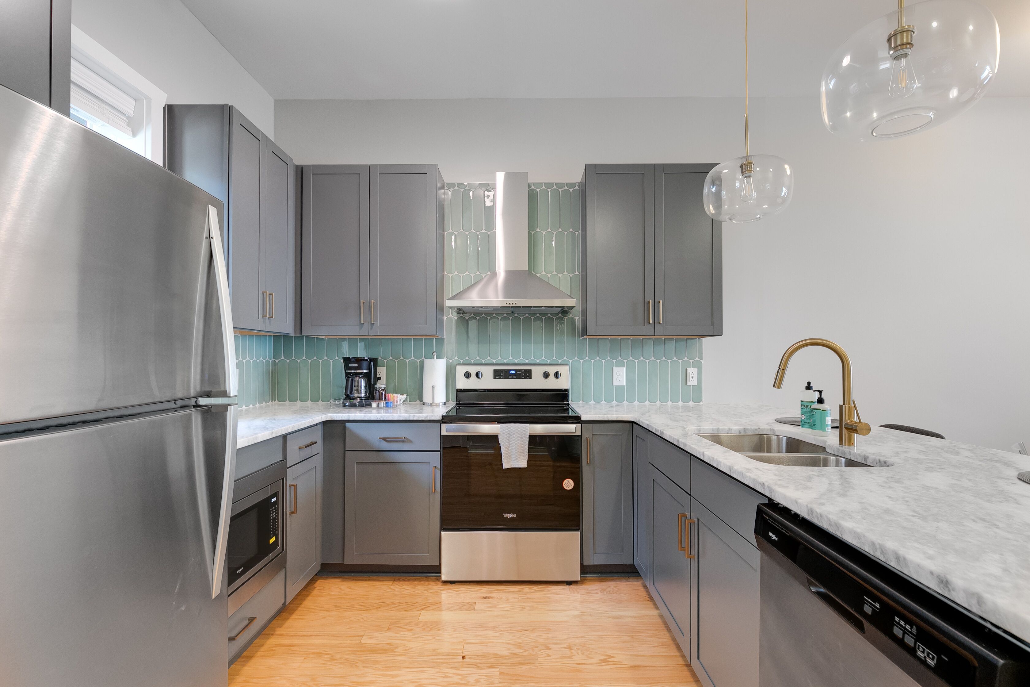 Une cuisine moderne dotée d’appareils électroménagers en acier inoxydable, de meubles de couleur grise, d’un îlot central et de luminaires suspendus.