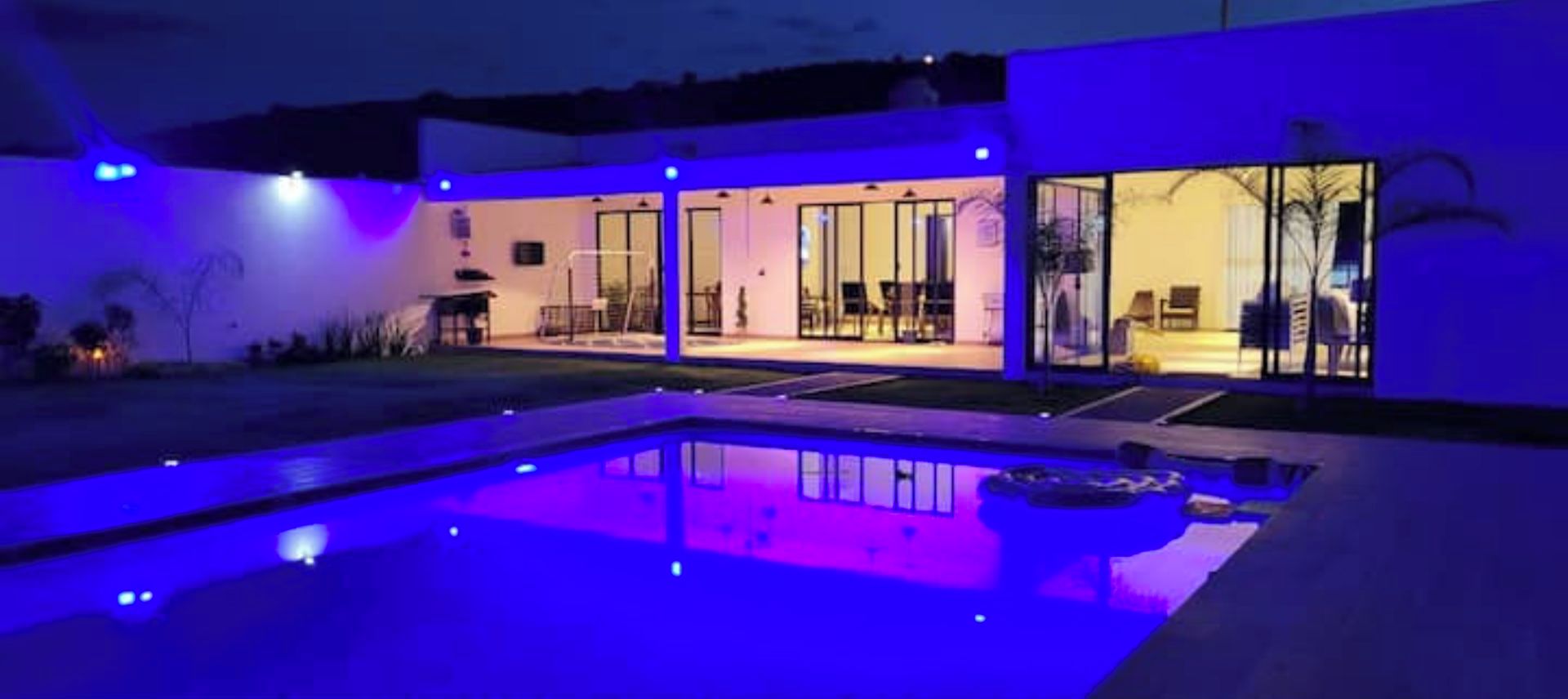 Une maison moderne dotée d’une piscine, de grandes portes vitrées et d’un intérieur bien éclairé.
