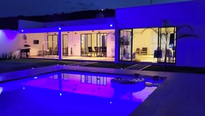 A modern house with a swimming pool, large glass doors, and a well-lit interior. - House Las Palmas (TICUMAN)