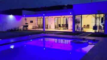 Une maison moderne dotée d’une piscine, de grandes portes vitrées et d’un intérieur bien éclairé.