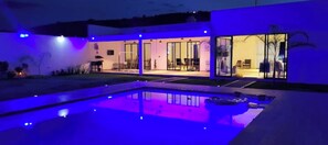 Et moderne hus med swimmingpool, store glasdøre og et godt oplyst interiør.