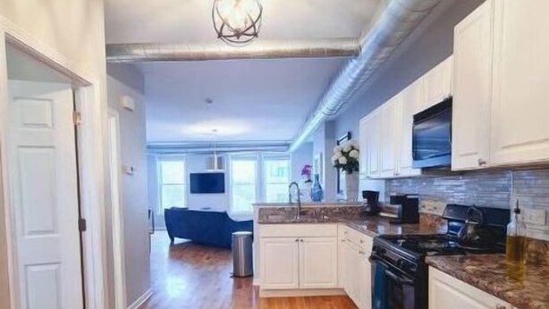 A spacious kitchen with wooden flooring, white cabinets, a built-in oven, and a microwave. - Medical District Gem III (Chicago)