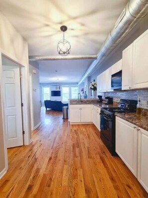 A spacious kitchen with wooden flooring, white cabinets, a built-in oven, and a microwave.