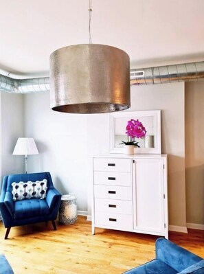 A modern living room with a blue armchair, a white cabinet, and a hanging pendant light.