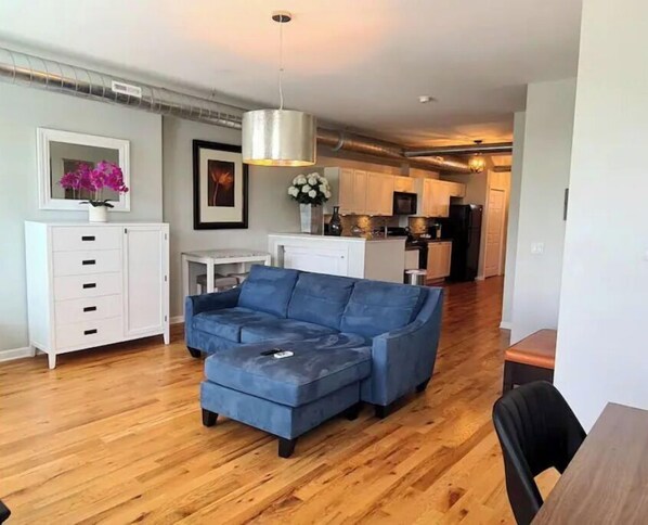 A modern living room with a blue sectional sofa, a white cabinet, and a dining area with a wooden table.